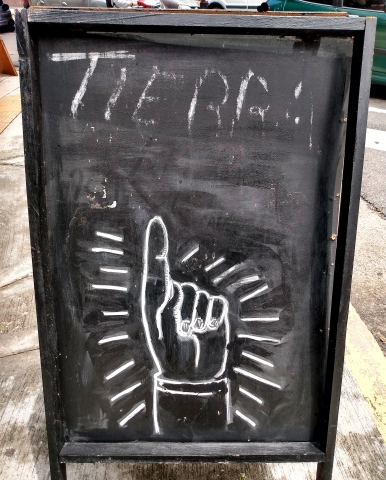 Blackboard standing on street with 'Tierra' written on it and hand drawn pointing upwards to it